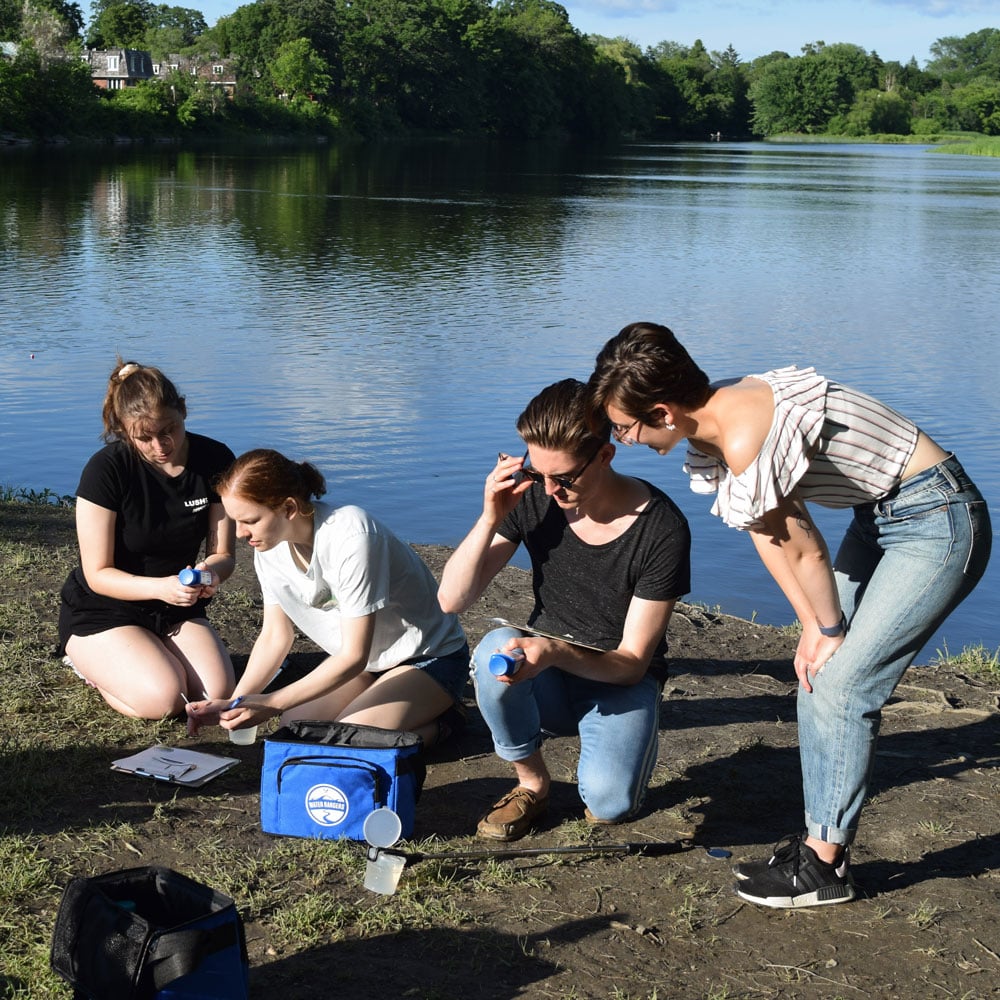 A group of water testers taking a water quality measurement, including water temperature. They are using a Water Rangers testkit