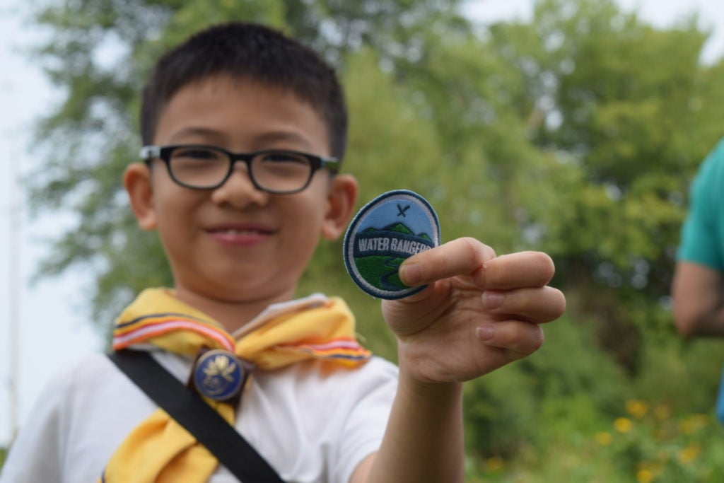 A child holding a Water Rangers badge. Supporting Water Rangers helps expose children like him to water testing!