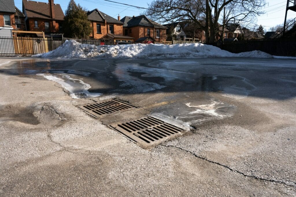 Snow melts into a drain on the ground. Road salts are visible next to the drain.