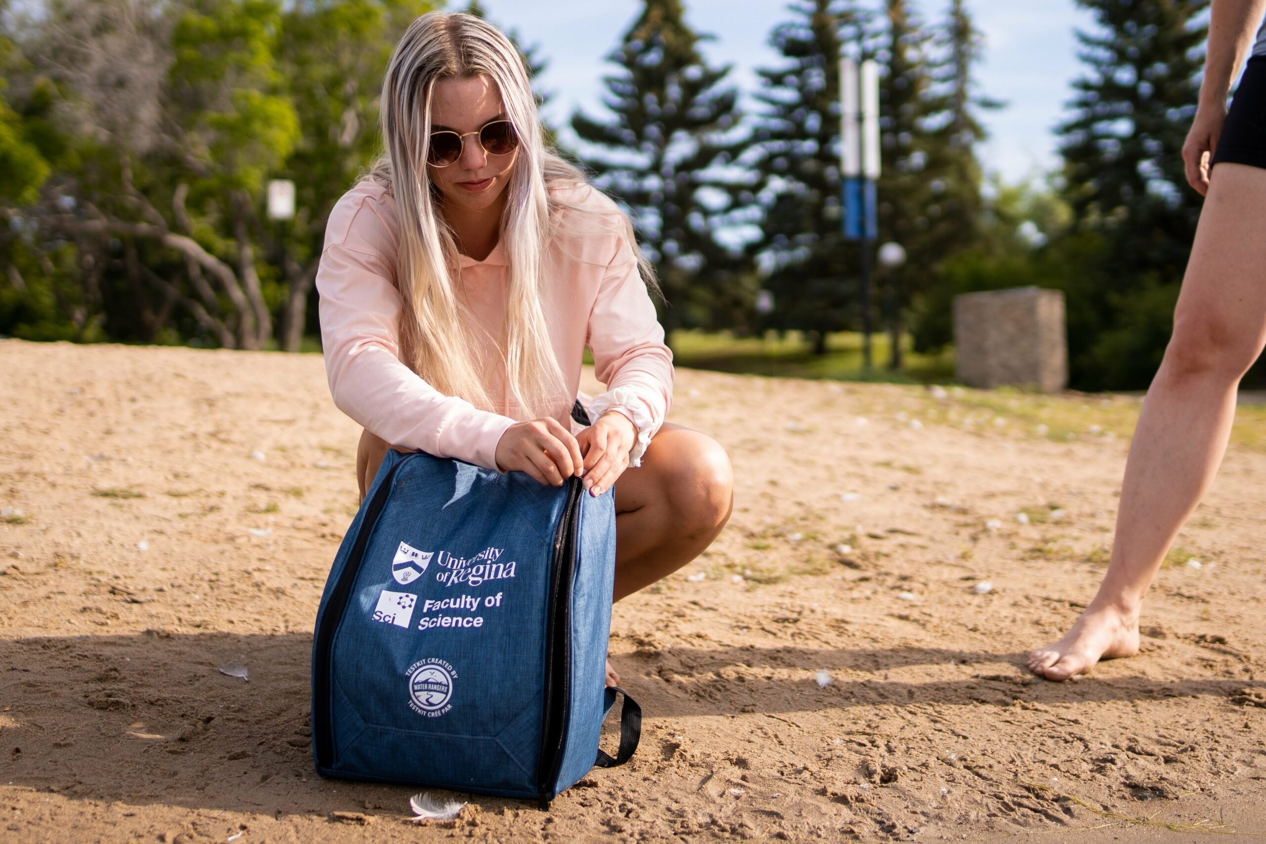 Woman with long blond hair and sunglasses unzipping a water testkit bag